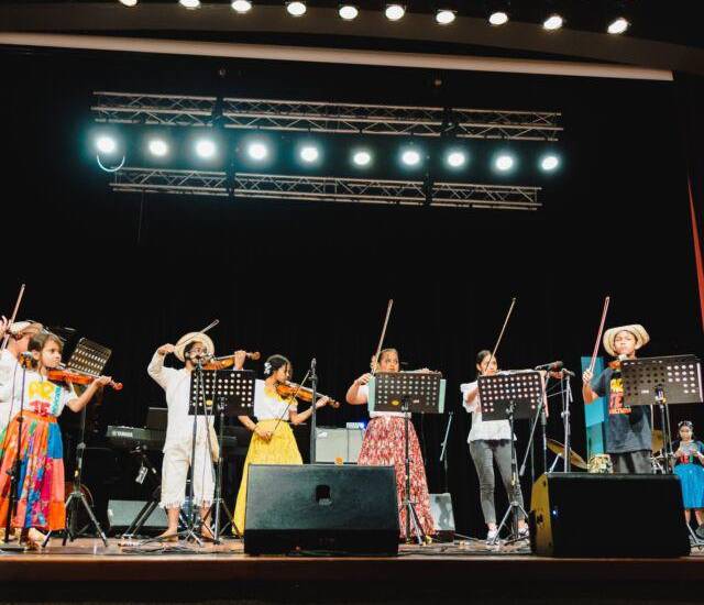 ML | Niños tocan diferentes instrumentos musicales en un escenario.