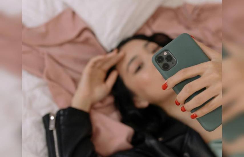 Una mujer acostada en una cama sosteniendo un celular.