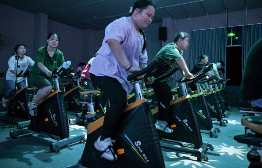 This photo taken on October 23, 2024 shows Yang Chi'ao (C) exercising at a weight loss camp in Chengdu, in China's southwestern Sichuan province. - Yang Chi'ao takes her place next to gym equipment and waits to be called by an instructor at a weight-loss camp in China, where over half of adults are overweight. Boasting strict daily exercise regimens, mandatory trips to the scale and rigid surveillance to guard against snacking, the facilities have popped up across China as it grapples with a growing obesity crisis. (Photo by Hector RETAMAL / AFP) / TO GO WITH 'CHINA-HEALTH-OBESITY, FOCUS' BY ISABEL KUA