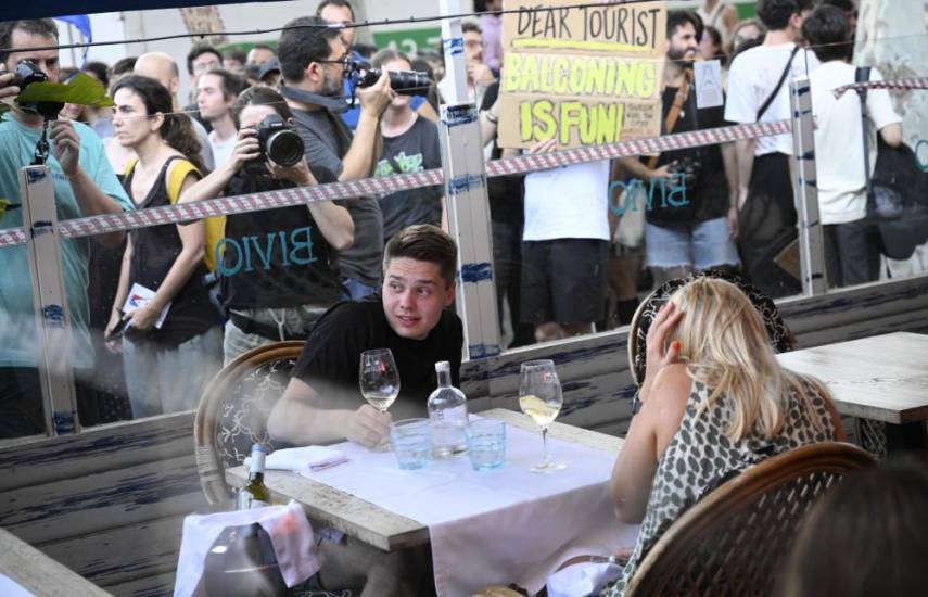 Demonstrators put symbolic cordon on a bar-restaurant window during a protest against mass tourism on Barcelona's Las Ramblas alley, on July 6, 2024. - Protests against mass tourism have multiplied in recent months across Spain, the world's second-most visited country. (Photo by Josep LAGO / AFP)
