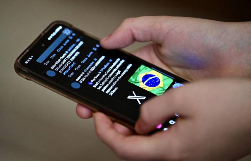 A Brazilian user of the social network X, formerly Twitter, browses posts on a cell phone in Brasilia on August 31, 2024. - Despite the court order to block X throughout Brazil, issued by Supreme Court judge Alexandre de Moraes, some users are still able to access the social network's pages in the country. (Photo by EVARISTO SA / AFP)